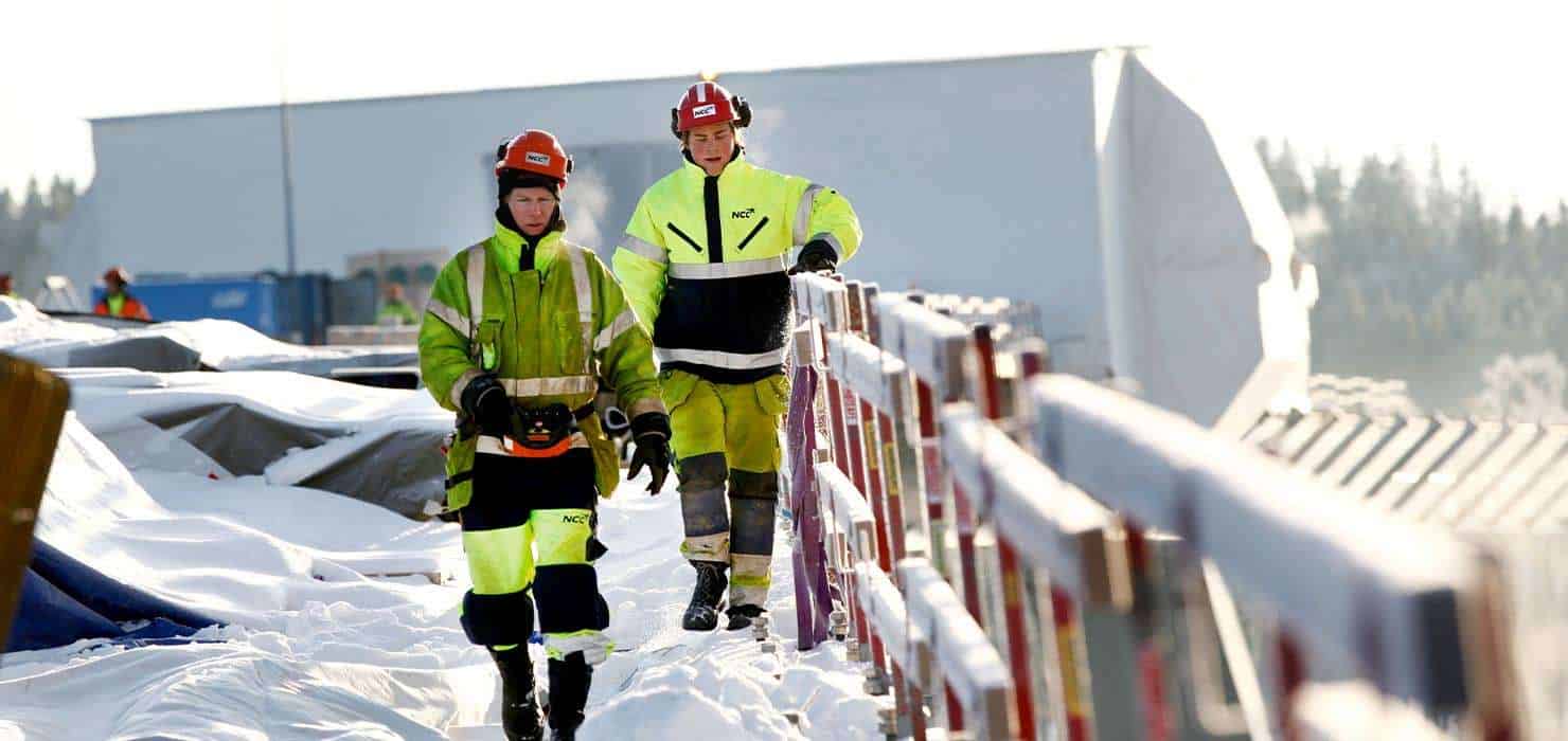 Emergency workers in high-visibility gear walking through snowy construction site, safety in winter.