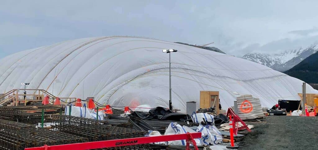 Climber and rescue equipment outside a large temporary shelter, prepared for mountain rescue operations.