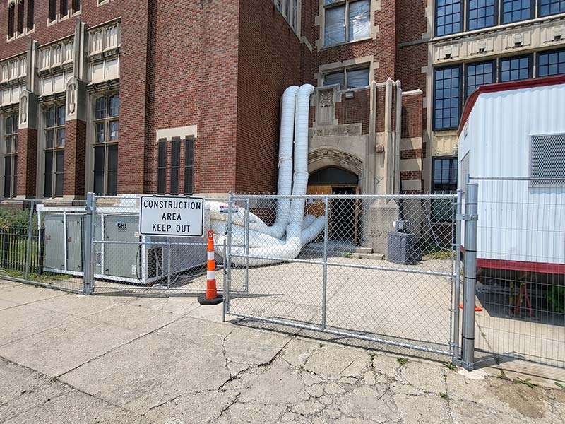 Construction area with safety fencing and pipes outside residential building.