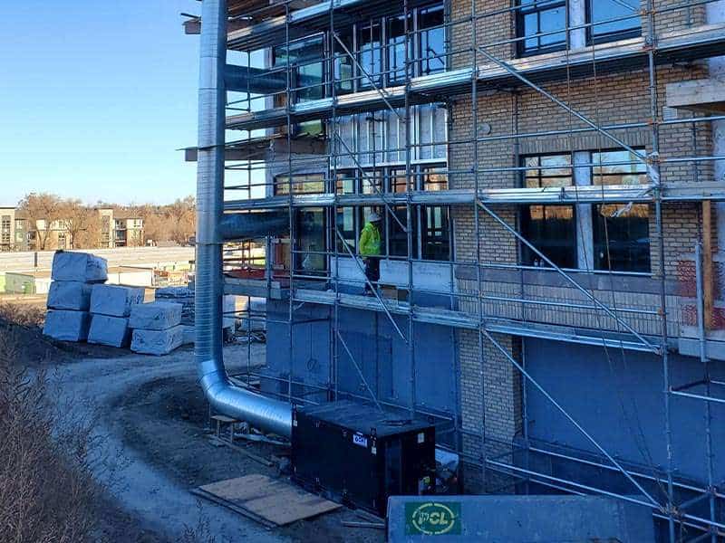 Construction site of residential building with scaffolding and worker in safety gear.