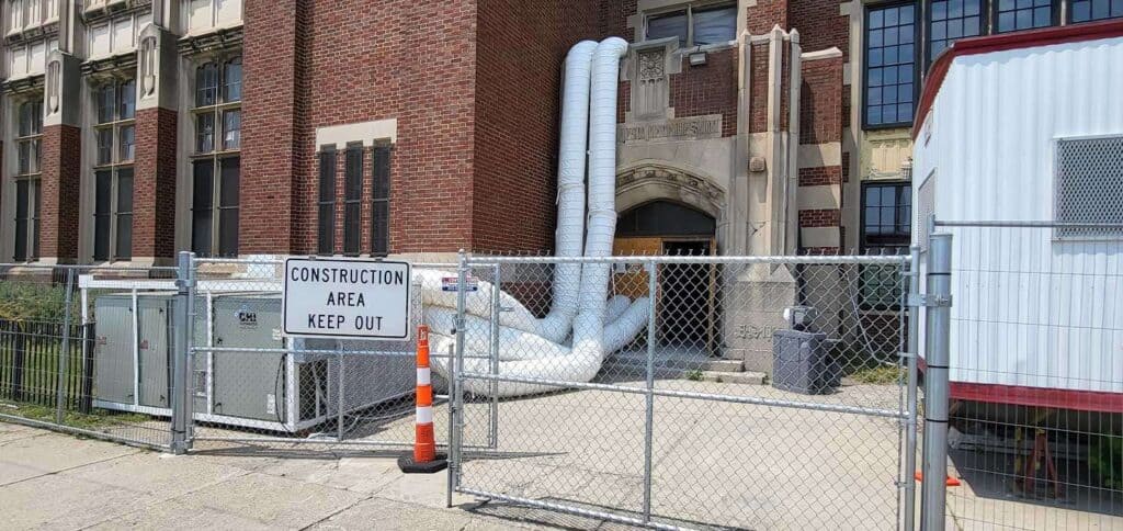 Construction site with fencing and pipes at historic building, under renovation, in an urban area.