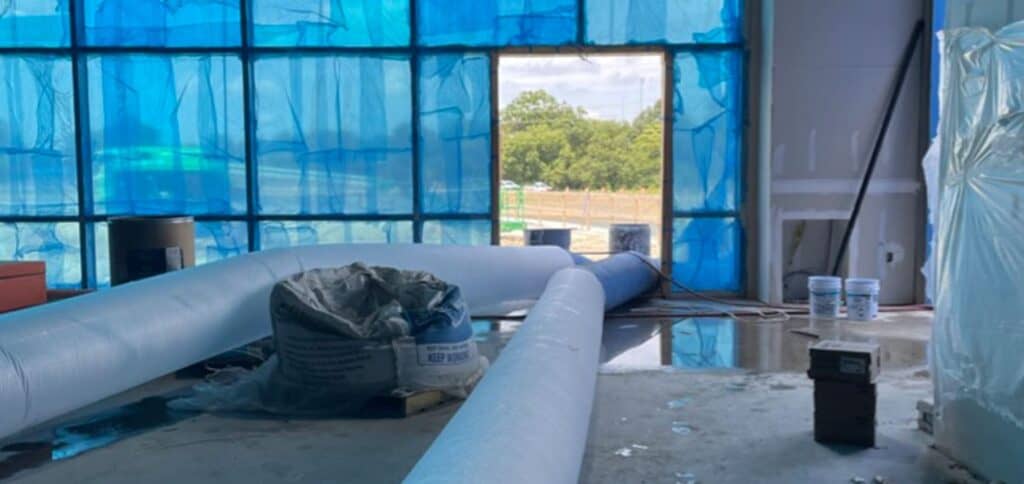 Insulated construction site with blue weather-resistant barrier and large pipes for climate control or plumbing.