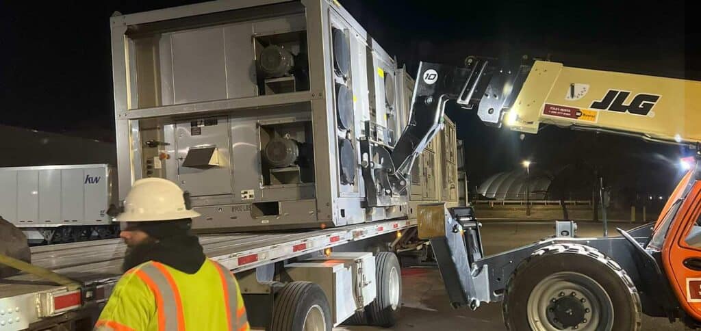 Heavy equipment transfering commercial HVAC units at night for property maintenance.