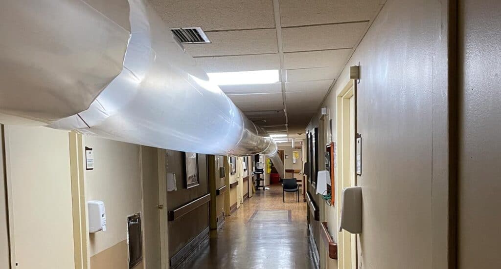 Large hospital corridor with medical equipment and ceiling ventilation duct, characteristic of healthcare facility environment.