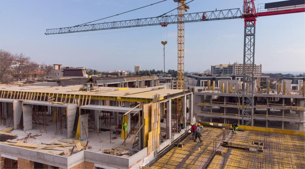 Steel and concrete building construction site with cranes and workers, new residential development under progress.