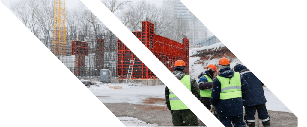 Construction site with workers in safety gear, winter weather, and building structures in progress.