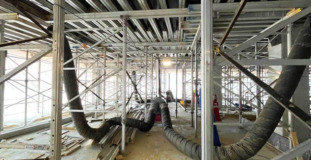 Flexible duct insulation in construction site under scaffolding, HVAC ductwork installation.