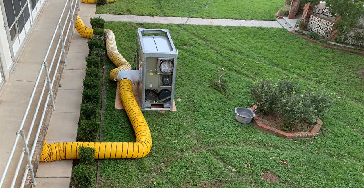 Flexible yellow ventilation duct connected to HVAC unit on green lawn, commercial property maintenance.