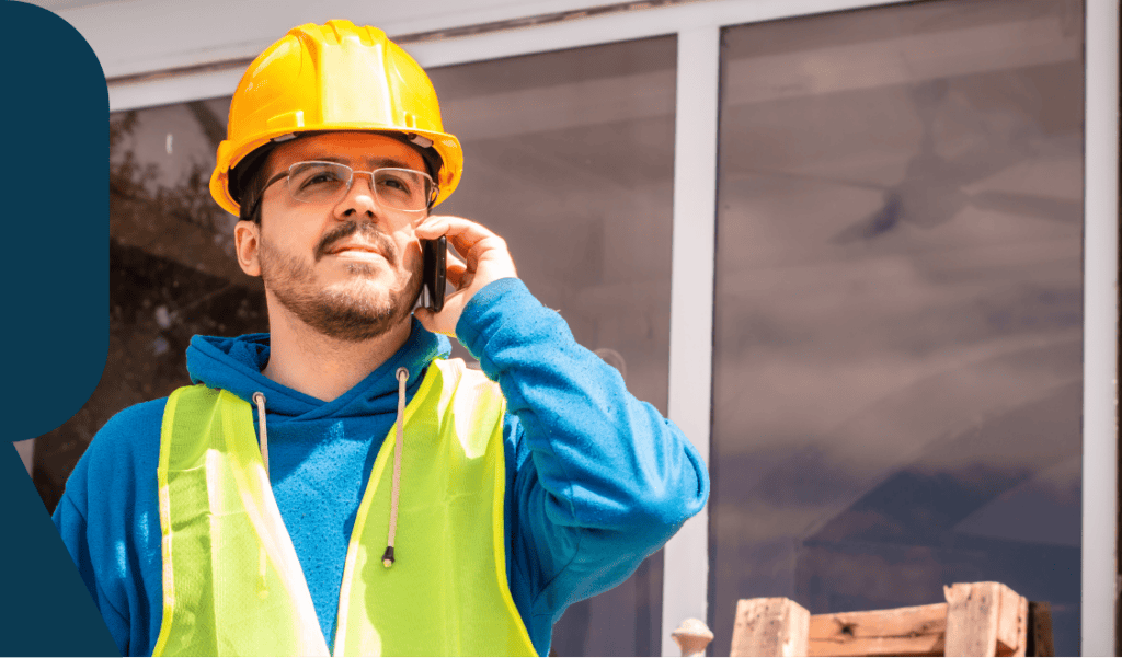 Hard hat construction worker talking on phone at rental property site in the US.