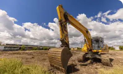 Excavator working on construction site with blue sky and clouds.
