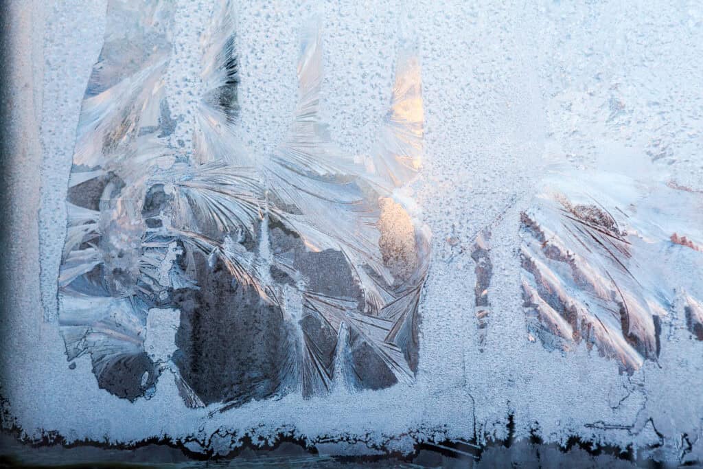 Frosted window with intricate ice crystal patterns, showcasing winter weather and cold climate conditions.