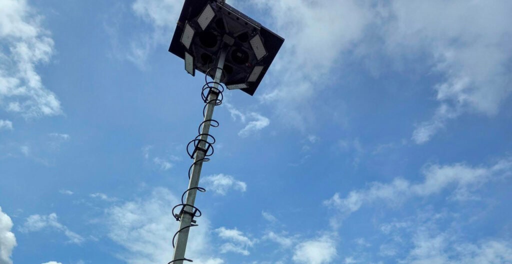 Solar-powered outdoor security camera on a tall pole under blue sky with clouds.