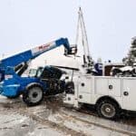 Mobile crane and utility truck with snow removal equipment in winter conditions.