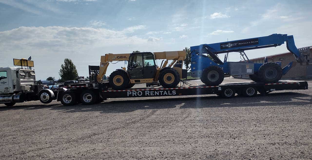 Heavy-duty telehandler being transported on flatbed trailer at a construction equipment yard.