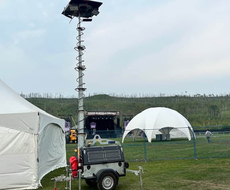 Weather monitoring equipment with solar-powered sensors and tall mast at outdoor event.