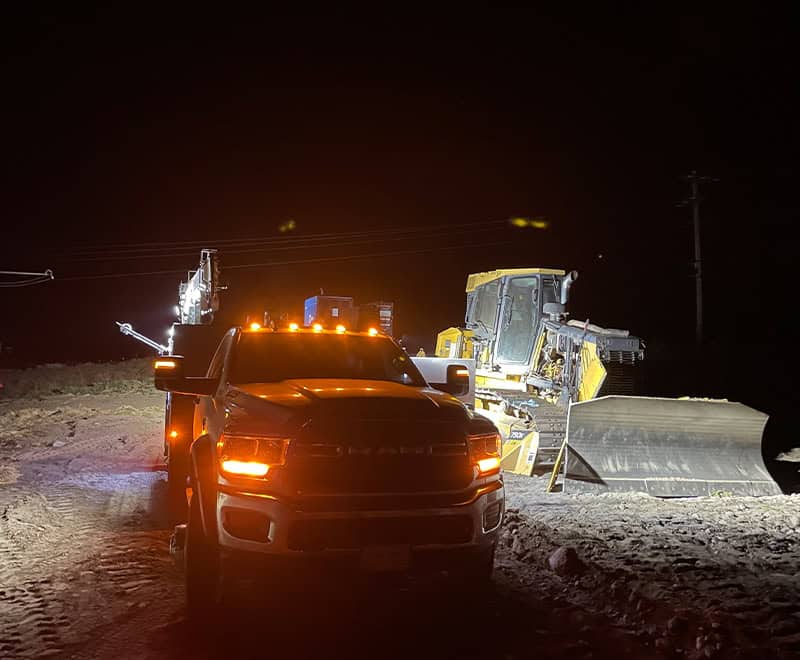 Construction equipment and trucks working at night on a road project.
