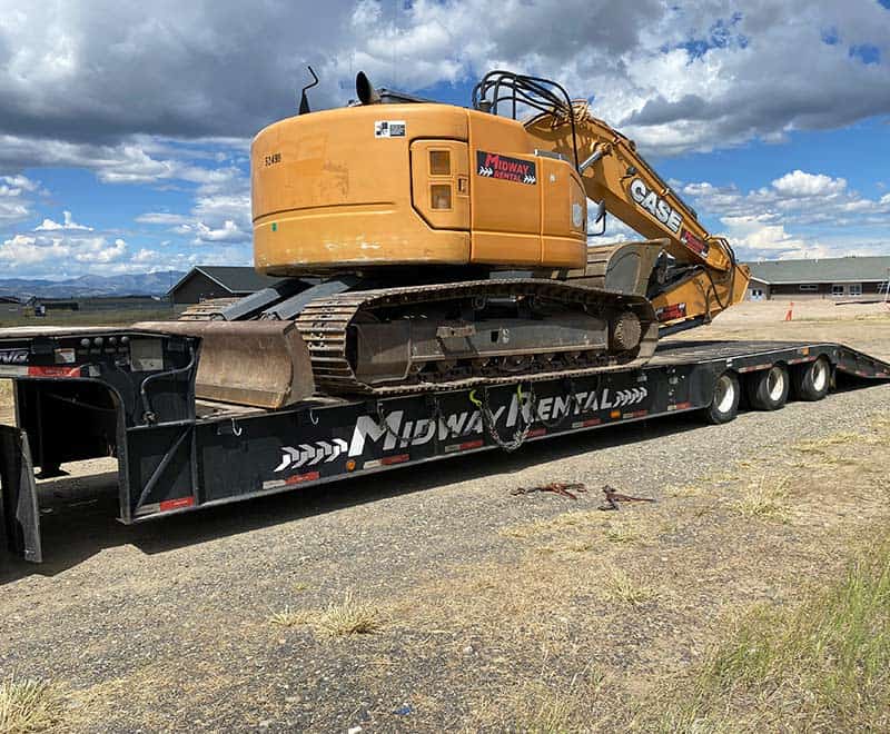 Excavator for rent on flatbed trailer at REIC Rentals, ideal for construction and heavy-duty project.