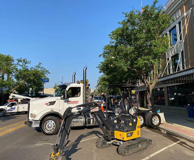 Construction equipment on a city street with buildings and trees in the background.