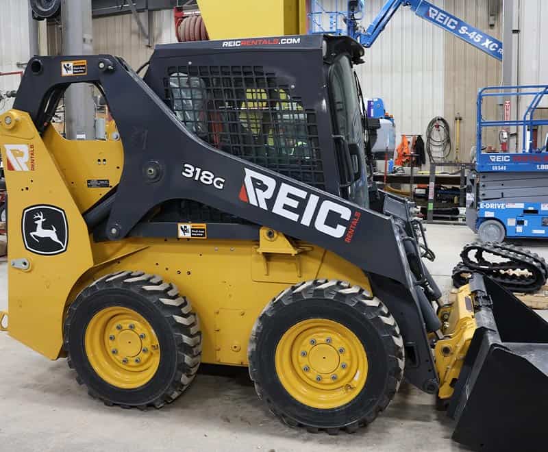 Yellow and black REIC skid steer loader with attachments at rental facility.