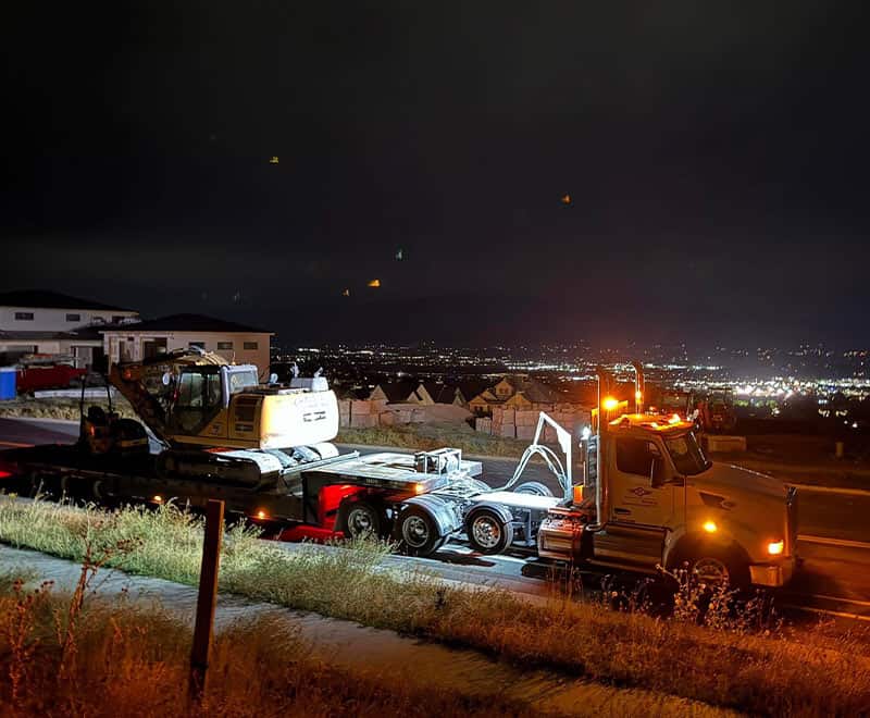 Construction vehicle at night on a hillside, illuminated by work lights.