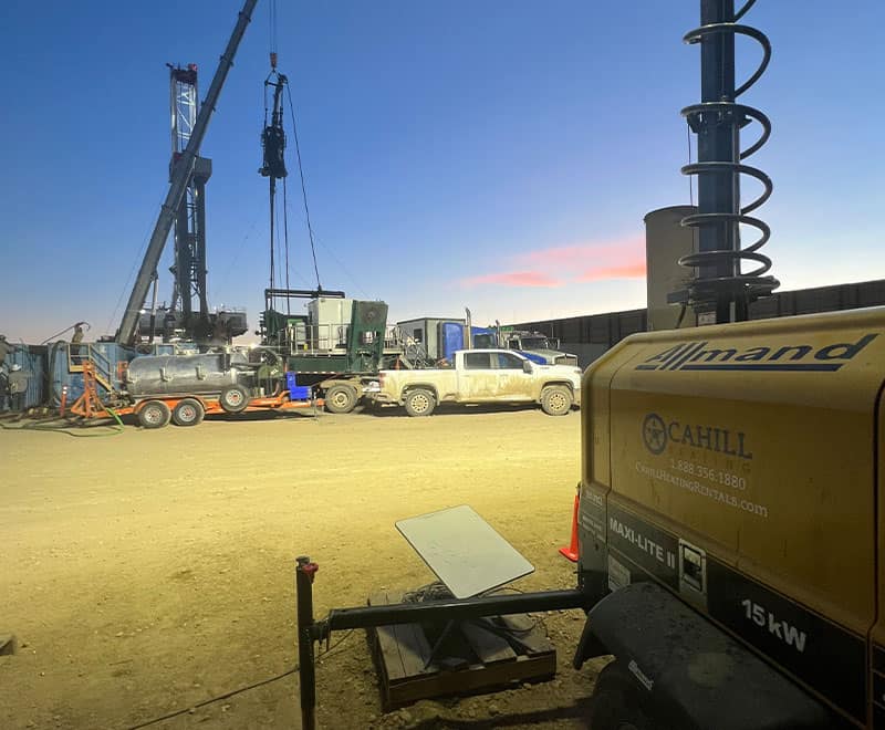 Construction site with drilling machinery, trucks, and equipment during dusk.