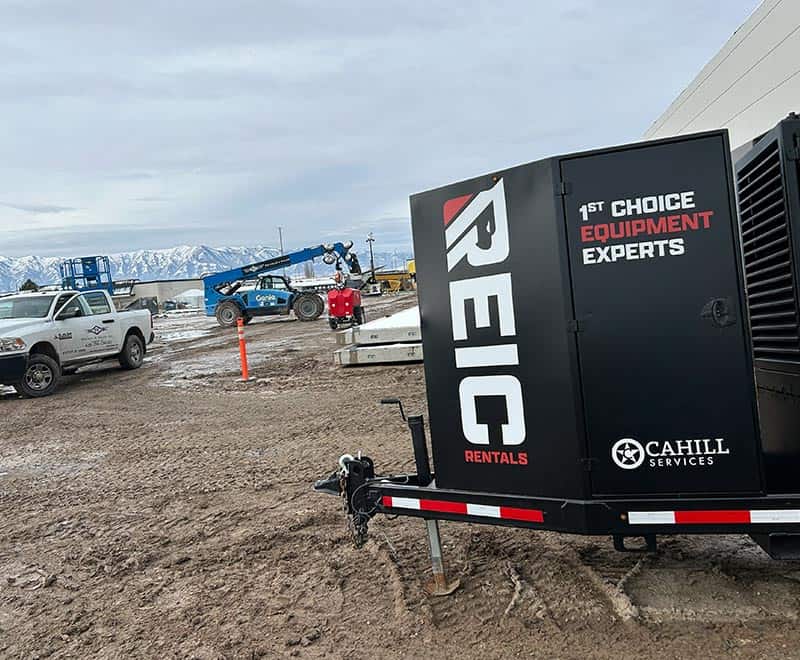 REIC Rentals equipment trailer with construction machinery at outdoor site.