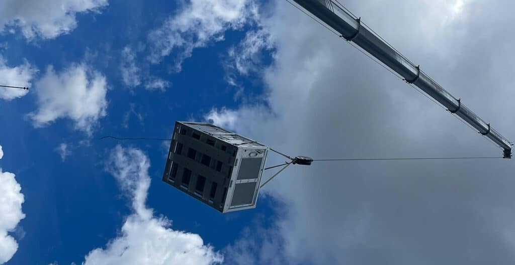 Crane lifting a large container against a blue sky with clouds.