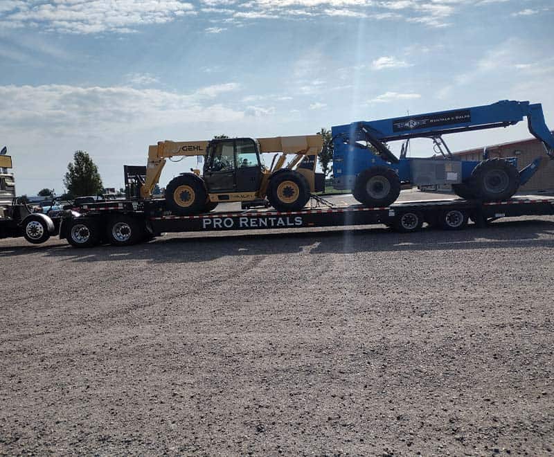 Construction machinery on flatbed trailer for rental in Ontario.