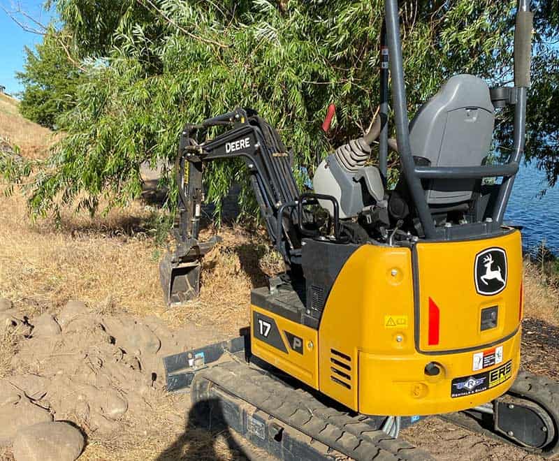 Small yellow John Deere mini excavator on a construction site near water.