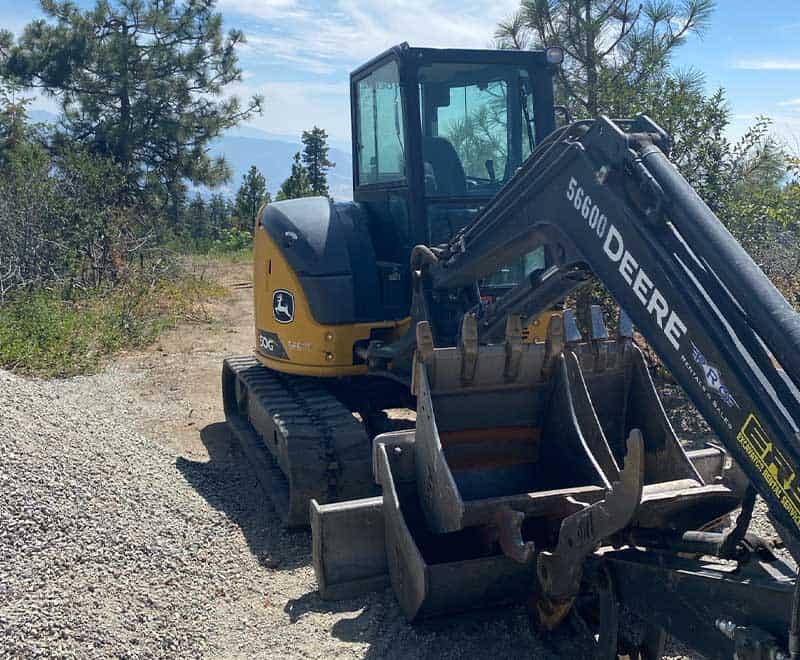 John Deere 56G Compact Excavator on a gravel path in a wooded area.