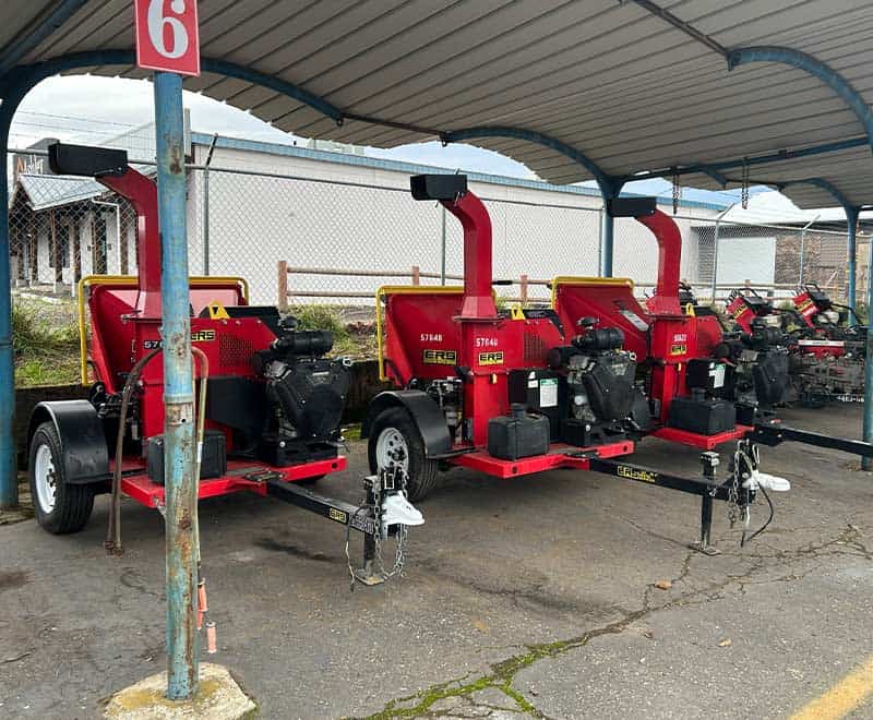 Multiple red industrial wood chippers lined up under a canopy at REIC Rentals.
