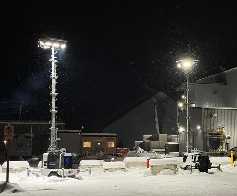 Snow-covered industrial site at night with bright floodlights illuminating the area.