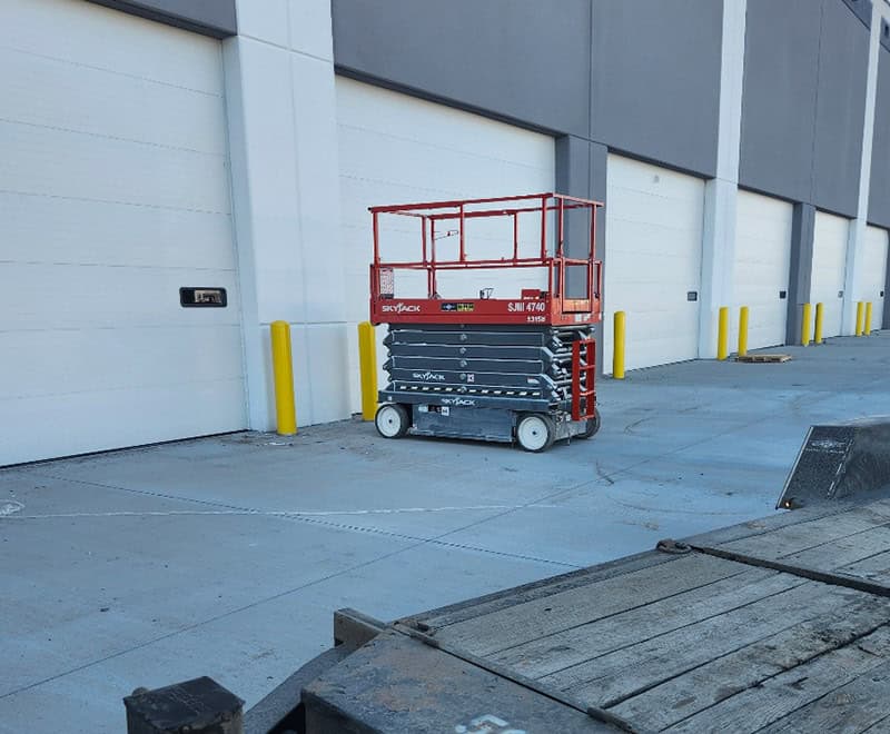 Scissor lift parked outside warehouse in Yakima for storage or maintenance.