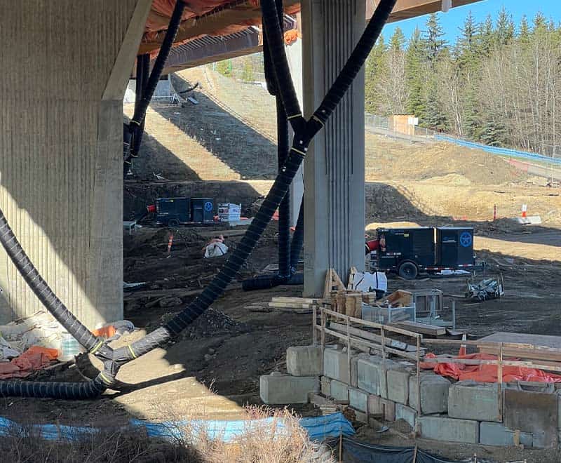 Construction site under bridge with equipment and workers in Red Deer area.