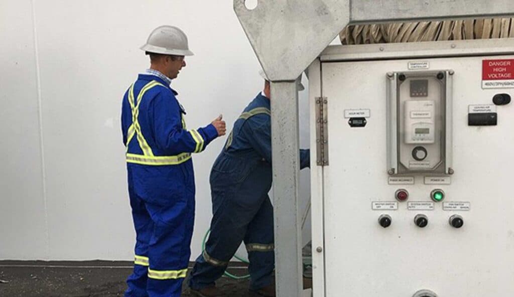 Workers inspecting electrical control panel in industrial setting.