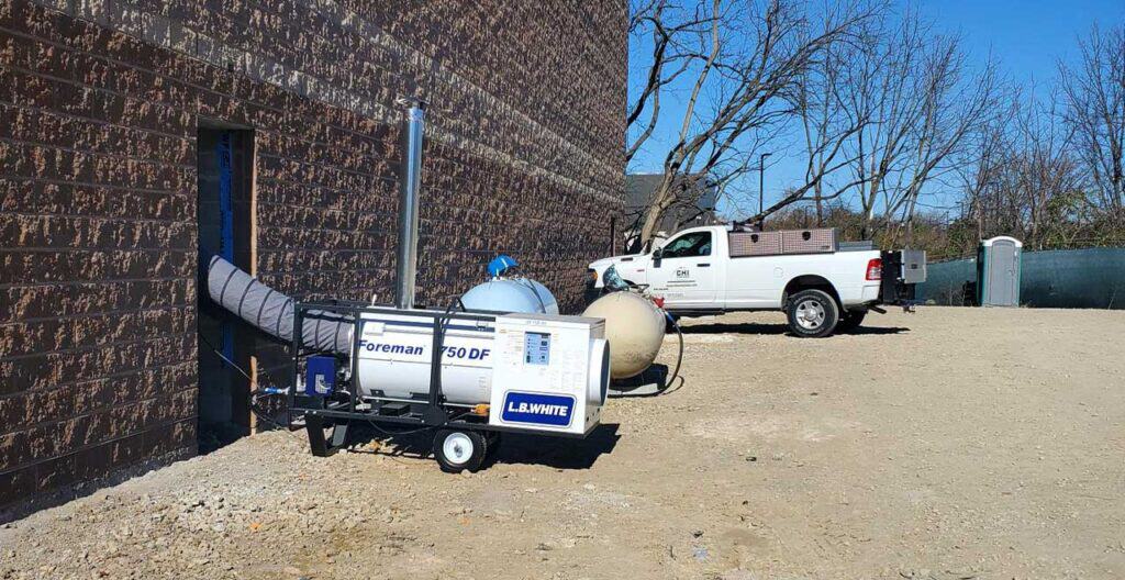 Industrial portable air filtration unit outside brick building with truck nearby.