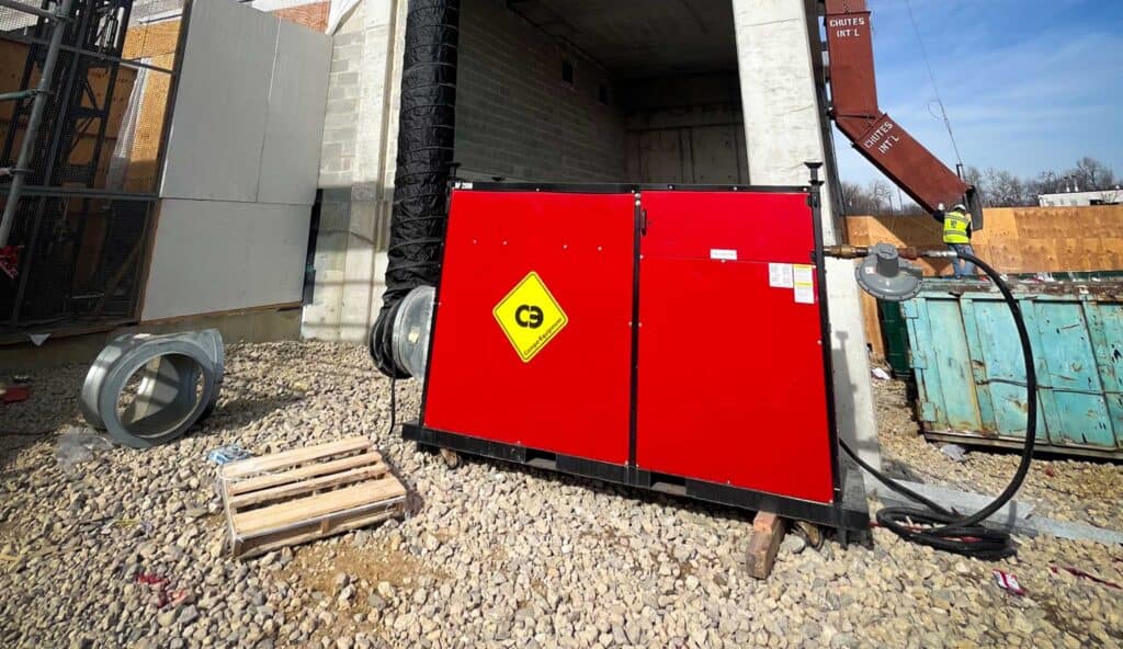 Red industrial generator on construction site with safety warning sign.