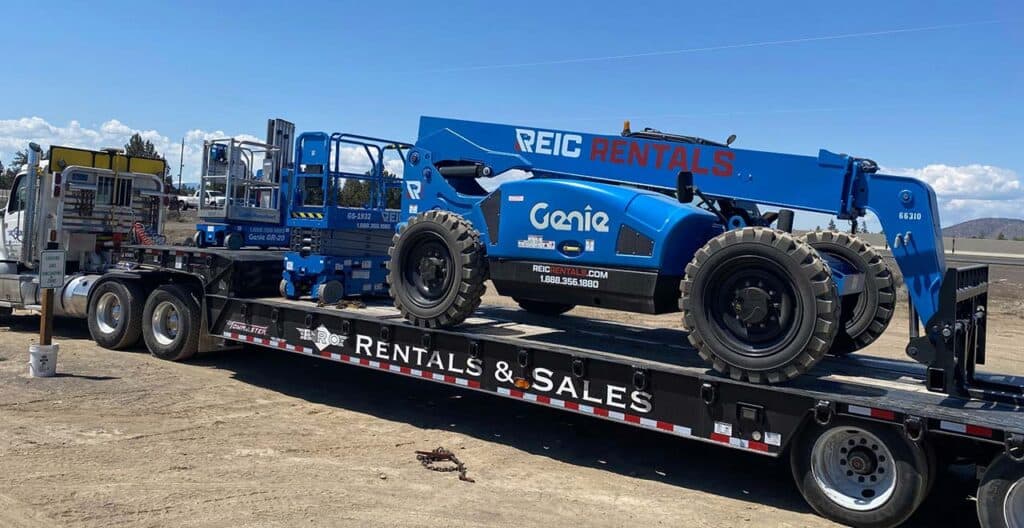 Heavy equipment transport truck with Genie telescopic boom lift on flatbed trailer.