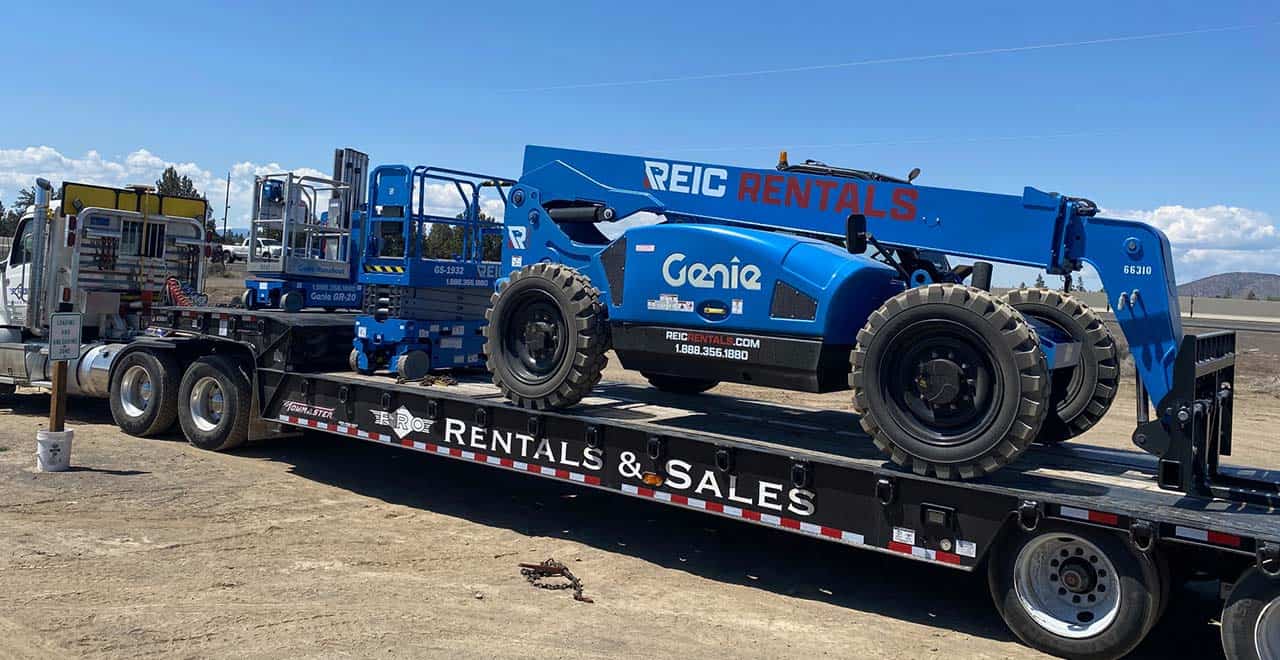 Heavy equipment transport truck with Genie telescopic boom lift on flatbed trailer.