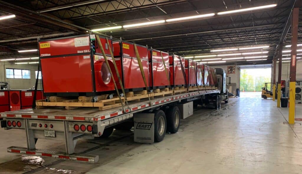 Large industrial equipment loaded on a flatbed truck inside a warehouse.