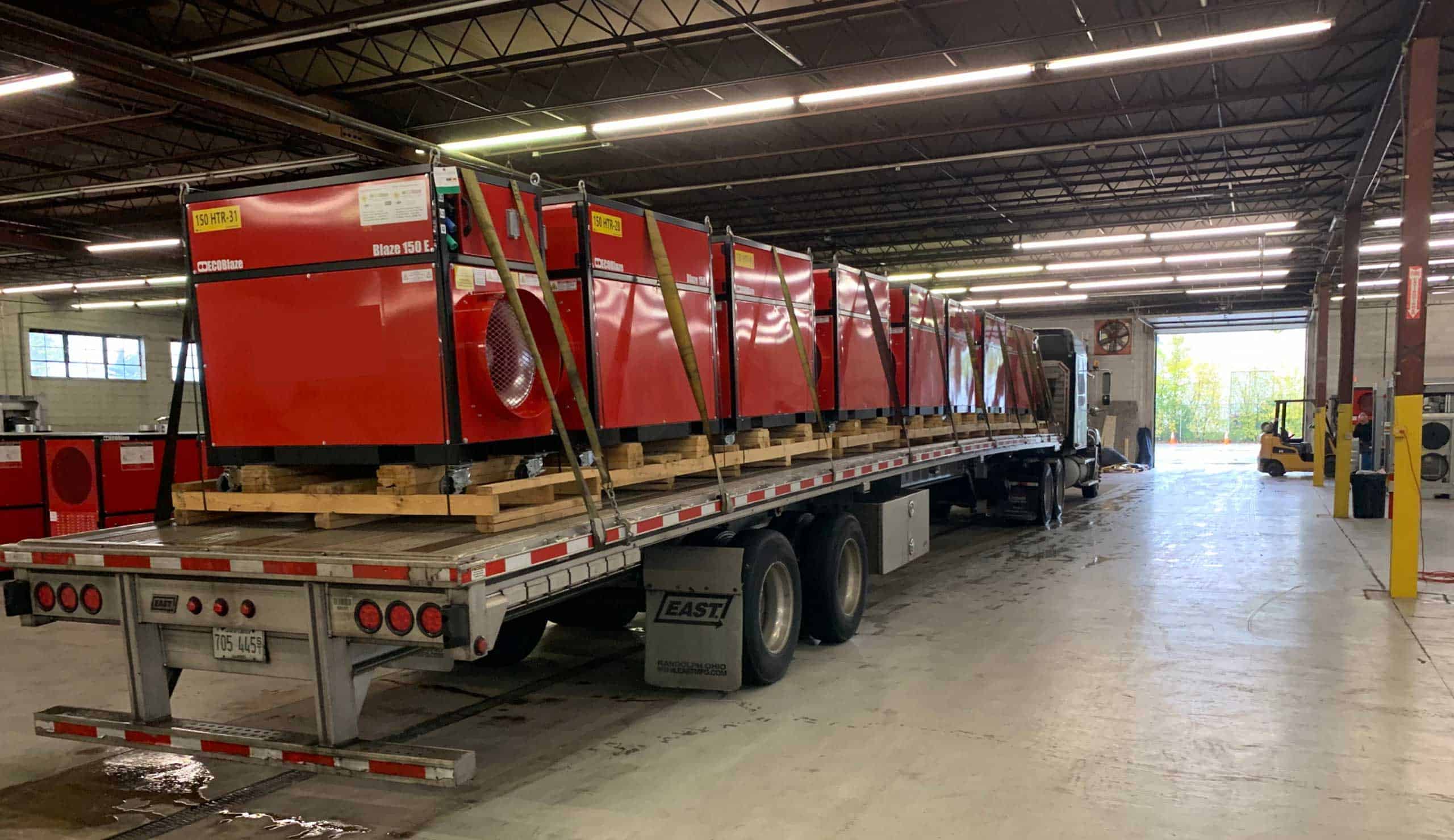 Large industrial equipment loaded on a flatbed truck inside a warehouse.