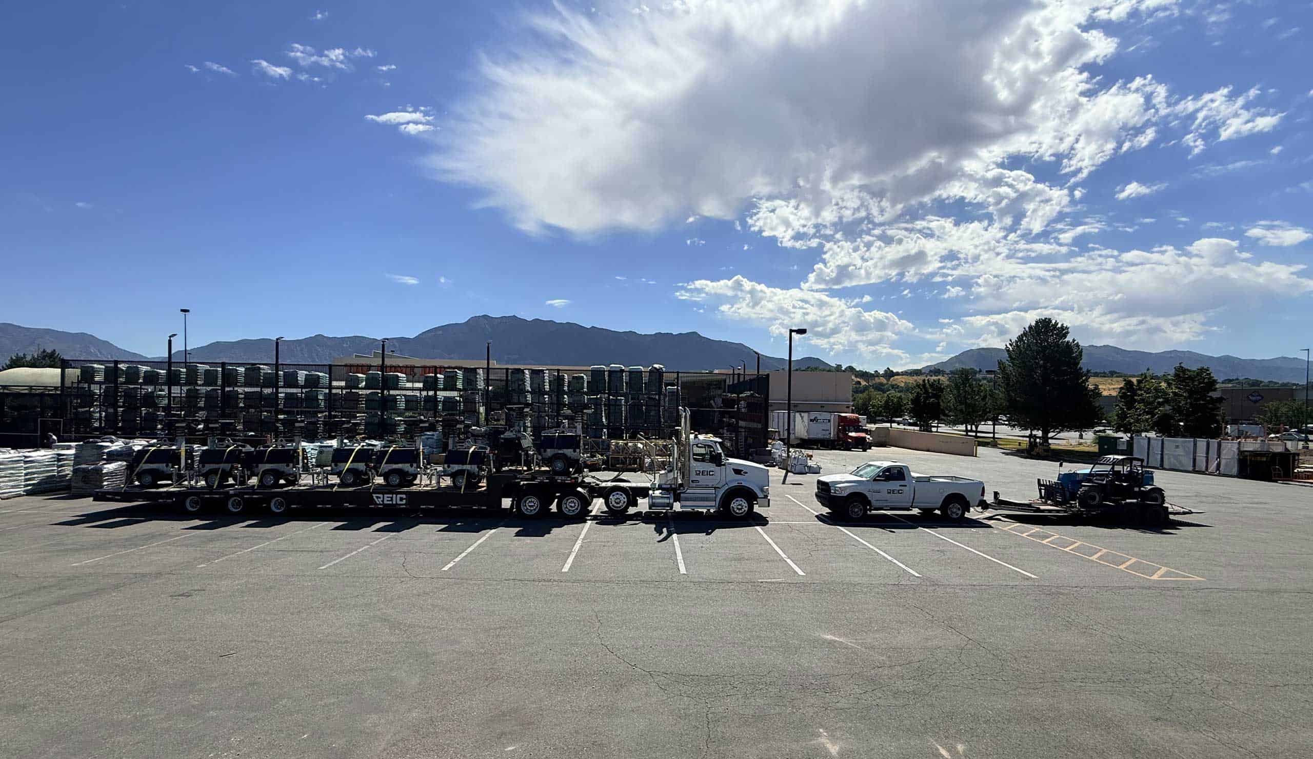 Large parking lot with trucks and cars under a partly cloudy sky.