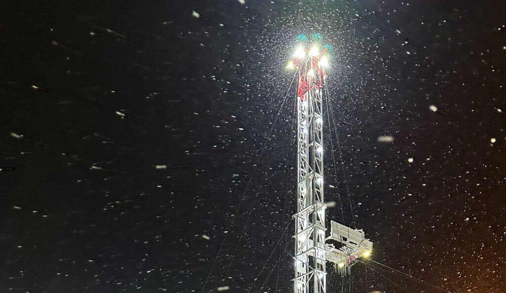 Cell tower illuminated at night with snow falling around it.