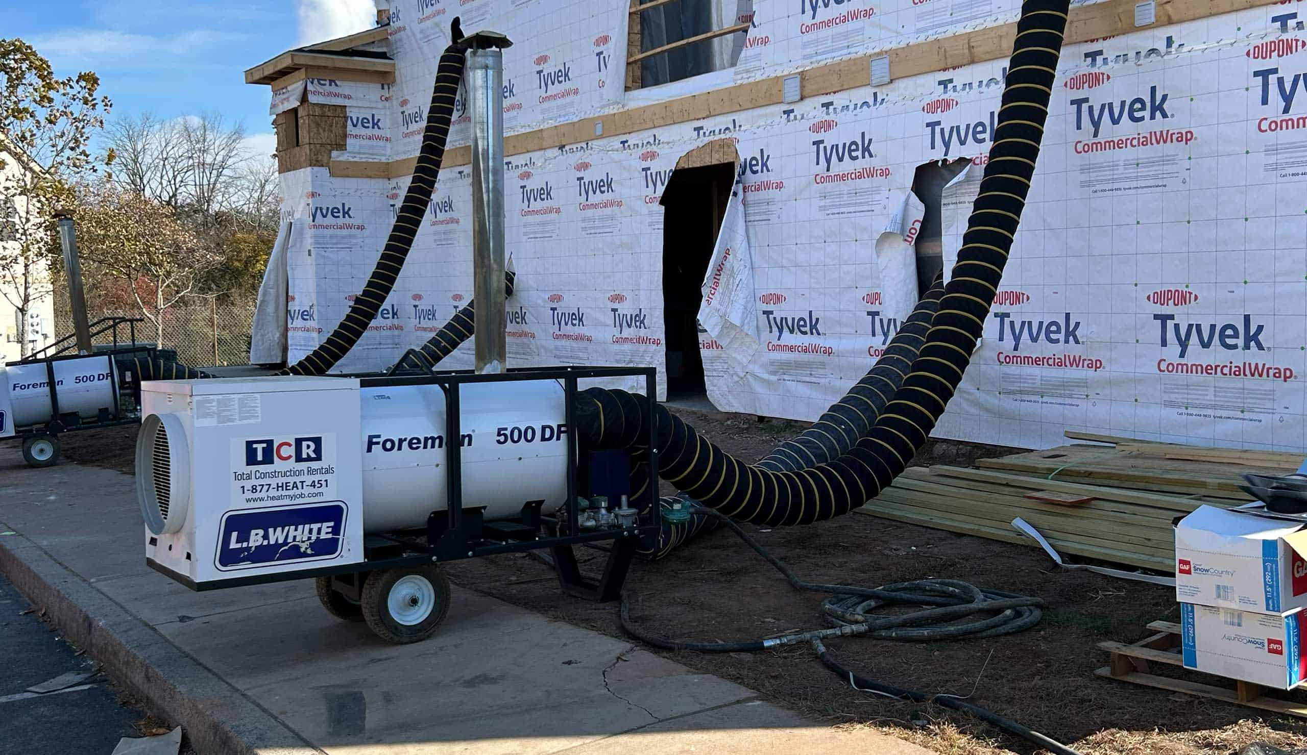 Winter construction site with HVAC hose and Tyvek-wrapped building under installation.